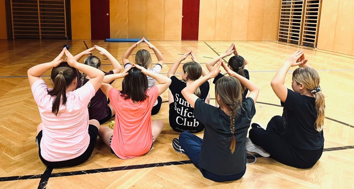 Kindergruppe sitzt im Kreis und formt eine Tanzfigur mit den Armen