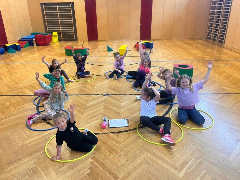 Kindergruppe sitzt mit Reifen im Kreis auf dem Hallenboden